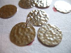 six silver and gold disc pendants sitting on top of a white cloth covered table