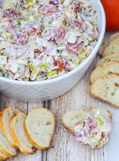 a white bowl filled with salad next to slices of bread and an orange in the background