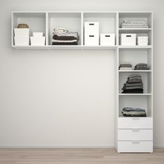 a white shelf with clothes and boxes on it in an empty room next to a wall