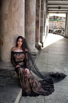 a woman sitting on the ground wearing a long black dress and veil over her head