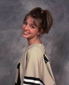 a young woman is smiling and wearing a baseball uniform with her hair in a bun