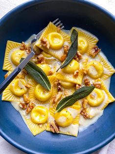 a blue plate topped with ravioli covered in cheese and nuts next to a fork