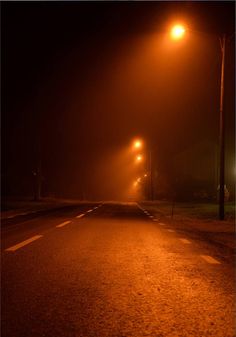 an empty road at night with street lights shining on it and fog in the air