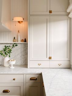 a kitchen with white cabinets and marble counter tops, gold handles and brass pulls on the cupboards