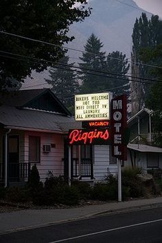 a motel sign is lit up in front of some houses and trees with mountains in the background