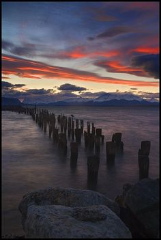 the sun is setting over an ocean with old wooden posts sticking out of the water