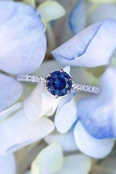 a blue diamond ring sitting on top of white flowers