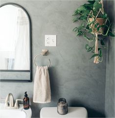 a white sink sitting under a bathroom mirror next to a green leafy wall hanging