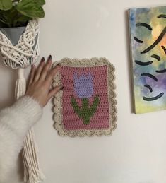 a woman's hand is touching a crocheted square with flowers on it