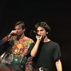 two young men singing into microphones on stage