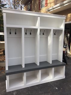 a bunch of white shelves sitting next to each other in front of a house with hooks on them