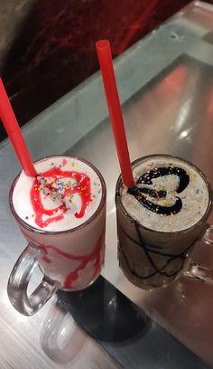 two drinks are sitting on a table with red straws in them and sprinkles all over the cups