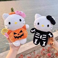 two crocheted hello kitty dolls holding pumpkins and jack - o'- lanterns