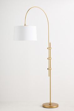 a gold floor lamp with a white shade on the base and a round light fixture