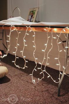 a person kneeling on the floor next to a table with lights strung across it and an ironing board in front of them