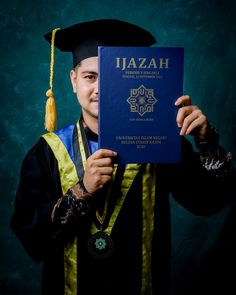 a man in graduation gown holding up a blue book with the word jazah on it