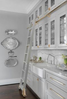 a ladder is in the middle of a kitchen with white cabinets and gold trimmings