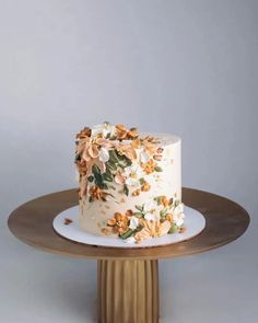 a white cake with flowers on it sitting on a wooden stand