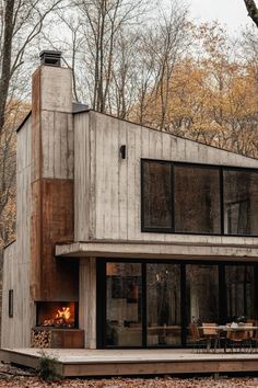 a modern house in the woods with an open fire place on the front and side