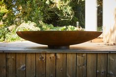 a large bowl sitting on top of a wooden table in front of a tree and bushes