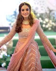 a woman in a pink and gold lehenga with her arms spread out to the side