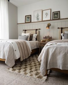 two twin beds in a bedroom with white walls and carpeted flooring, framed pictures on the wall above them