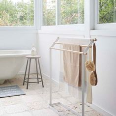 a bathtub and towel hanger in a bathroom with white walls, floor tiles and windows