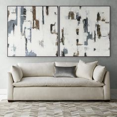 two abstract paintings hang on the wall above a couch in front of a white rug