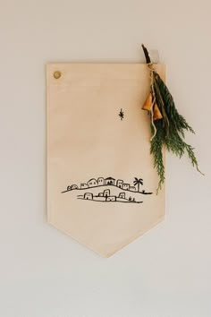 an embroidered banner hanging on the wall with a bell and evergreen sprig attached to it