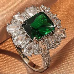 a ring with a green stone surrounded by crystal stones and diamonds on a gold cloth