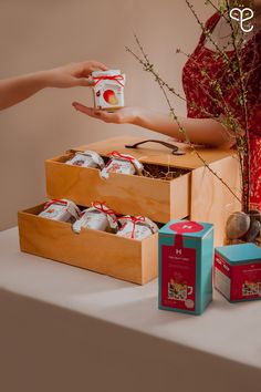 a woman holding a cup in front of two wooden boxes with teas on them