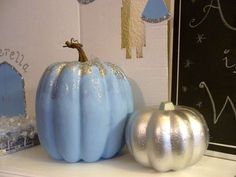 two blue and silver pumpkins sitting on top of a white shelf next to each other