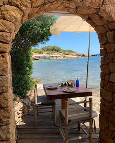 an outdoor dining area with table and chairs under an umbrella near the water's edge