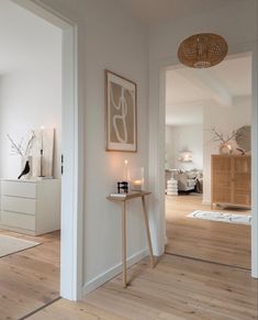 a living room with white walls and wood flooring next to a wooden table in front of a doorway