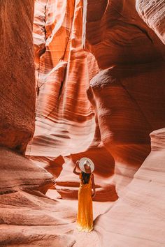 a woman in a yellow dress and hat walks through an area with large rock formations