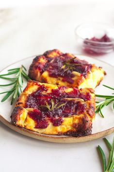 two pieces of bread with cranberry sauce on a white plate next to rosemary sprigs