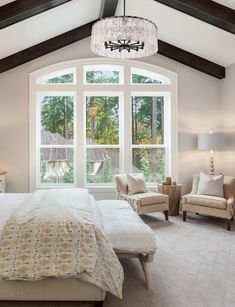 a bedroom with a large bed, two chairs and a chandelier hanging from the ceiling