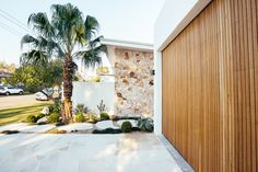 a wooden garage door next to a palm tree in front of a white wall and house