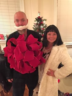 a man and woman standing next to each other in front of a christmas tree with red decorations on it