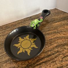 a small toy gecko sitting on top of a frying pan with the sun painted on it