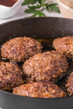 some meat patties are cooking in a pan