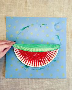 a paper plate with a slice of watermelon painted on it and a hand holding the piece