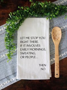 a tea towel with a quote on it next to a wooden spoon and green leaves