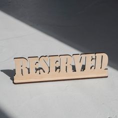 a wooden sign that says reserved on the side of a white wall with shadows coming through it