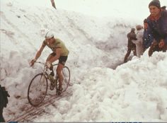 two men riding bikes down a snow covered mountain side trail with people watching from behind