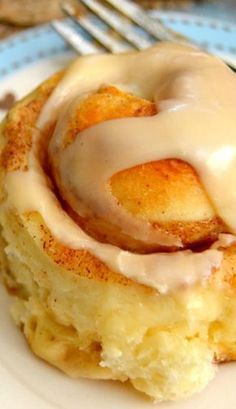 a cinnamon roll with icing sitting on top of a plate next to a fork