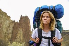 a woman with a backpack on her back standing in front of some rocks and mountains