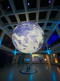 two people are standing in front of a large blue and white globe hanging from the ceiling