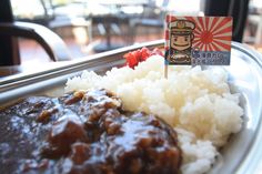 a white plate topped with rice and meat covered in gravy next to a flag