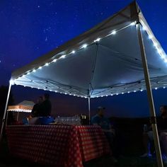 people are sitting under a tent with lights on it